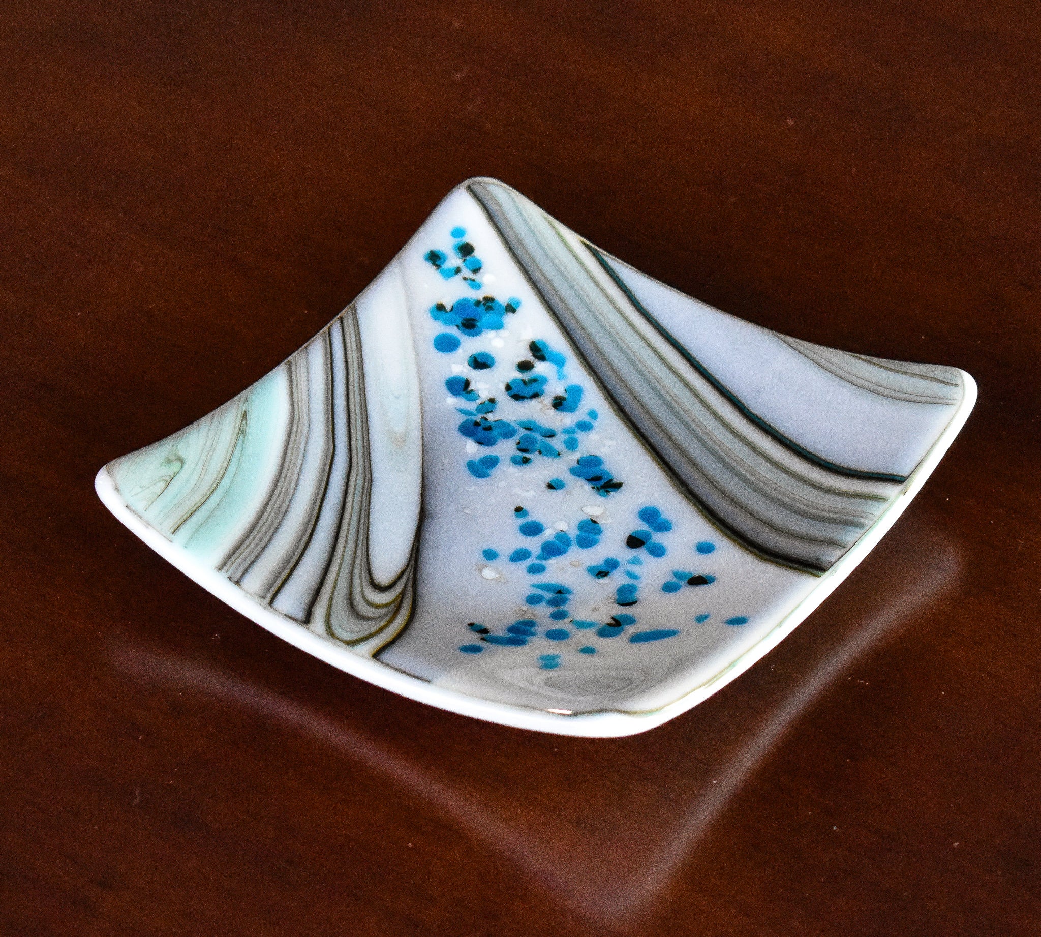 6&quot; square fused glass dish with swirl pattern and small flecks of white and blue glass, sitting on wood table