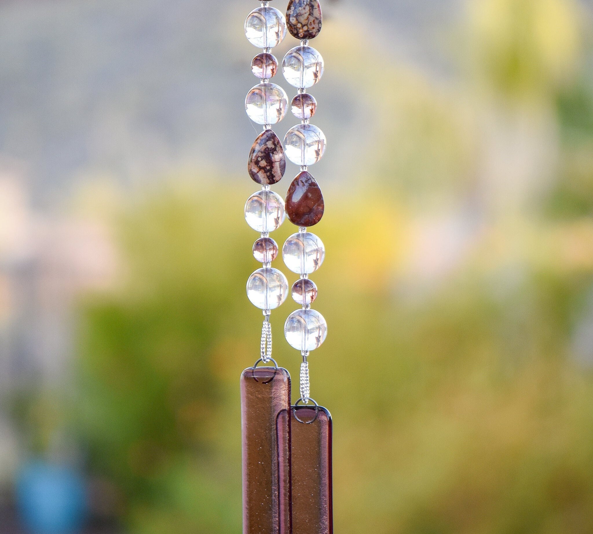 Tear-drop shaped rhyolite stones are strung with large clear glass beads and smaller pale purple beads. Anchored by two pieces of pale purple glass. Hanging from tree.