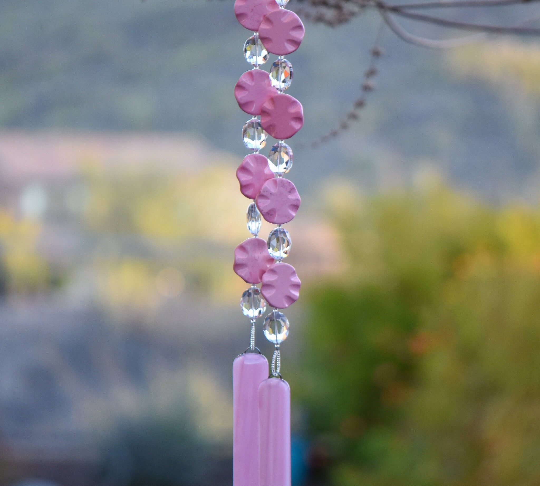 Pink magnesite stone beads shaped as wavy flat rounds are strung with glass crystal ovals and anchored by two pieces of pink fused glass. Hanging from tree.