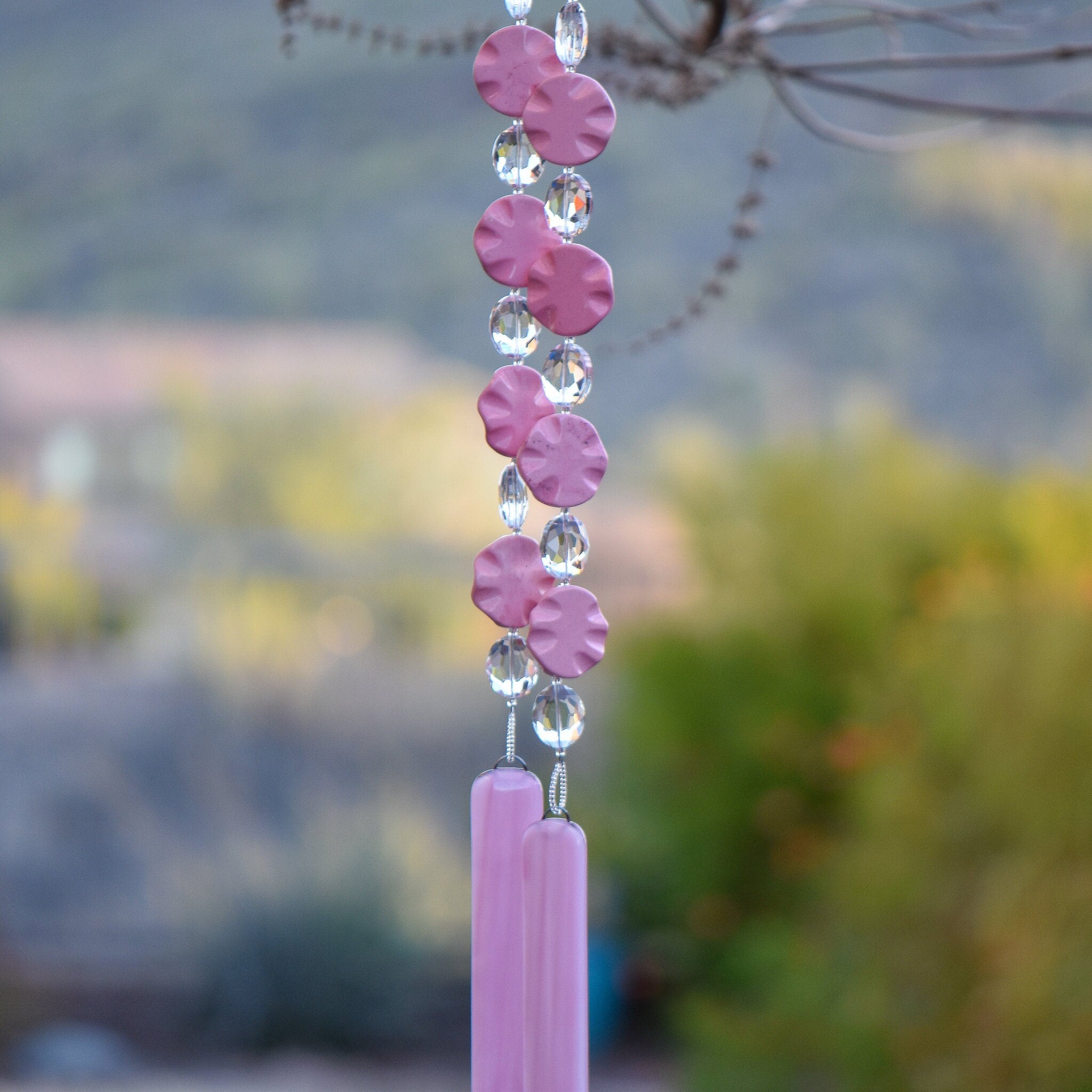 Pink magnesite stone beads shaped as wavy flat rounds are strung with glass crystal ovals and anchored by two pieces of pink fused glass. Hanging from tree.