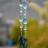 Very large solid glass aqua-colored beads paired with smaller clear glass beads, strung on wire and hanging vertically, anchored by two strips of sparkling green/aqua fused glass